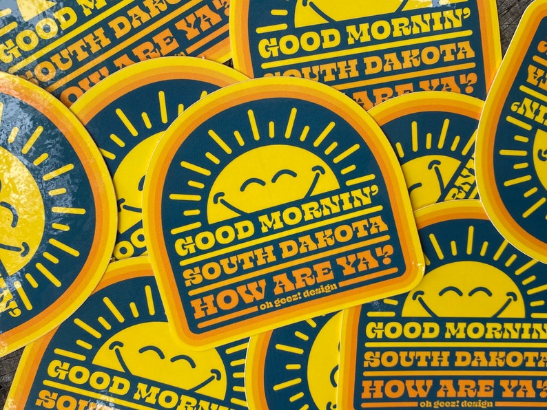 May include: A set of colorful stickers with a smiling sun and the text "Good Mornin' South Dakota How Are Ya?"  The stickers are printed on a dark blue background with yellow and orange accents.