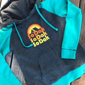 May include: A teal and gray hooded sweatshirt with a rainbow graphic and the text "SoDak SoDak SoDak" printed on the front.