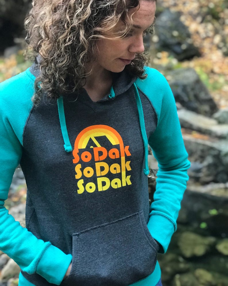 May include: A dark gray hooded sweatshirt with turquoise sleeves and a rainbow graphic with the text "SoDak SoDak SoDak" in orange and yellow.