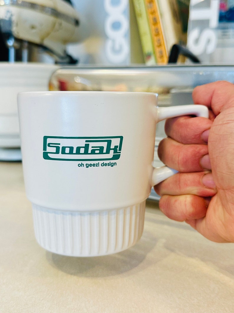 May include: White ceramic mug with a green logo that says "Sodak! oh geezl design"