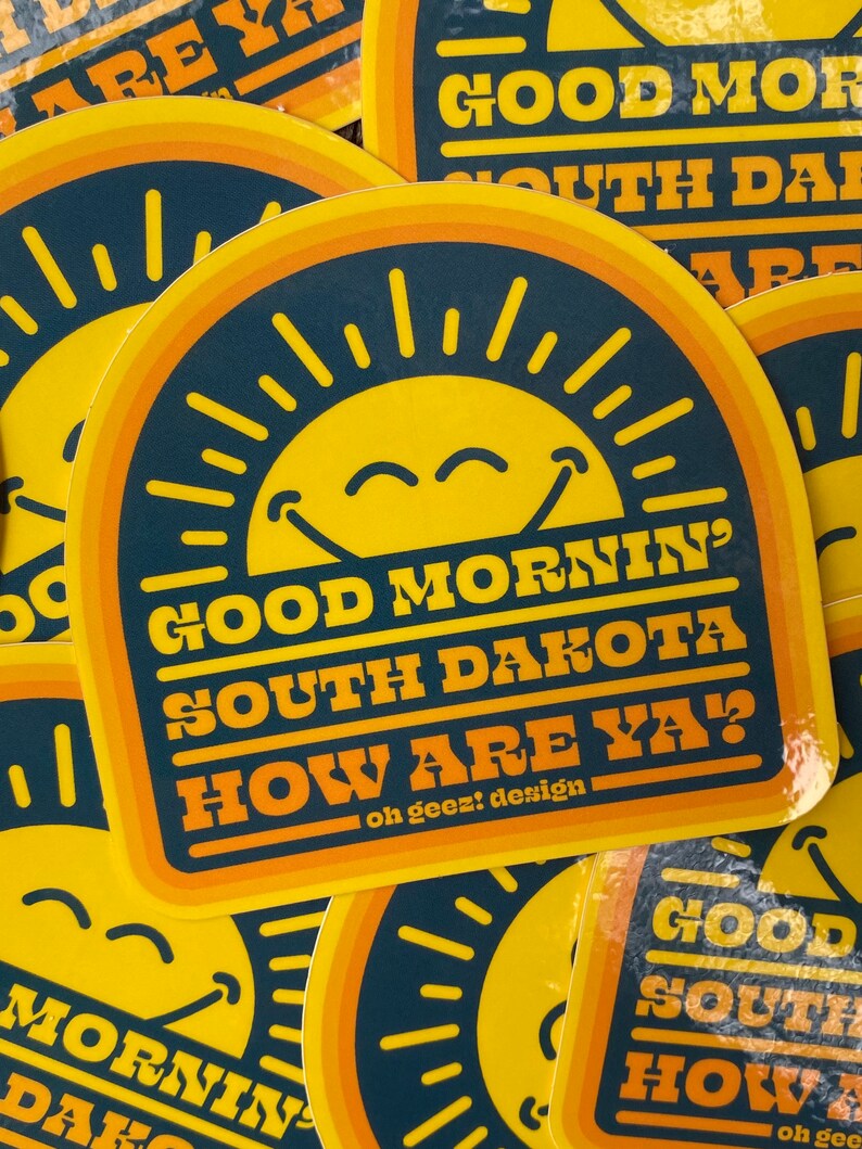 May include: A yellow and orange sticker with a smiling sun and the text "Good Mornin' South Dakota How Are Ya?" with the tagline "oh geez! design".