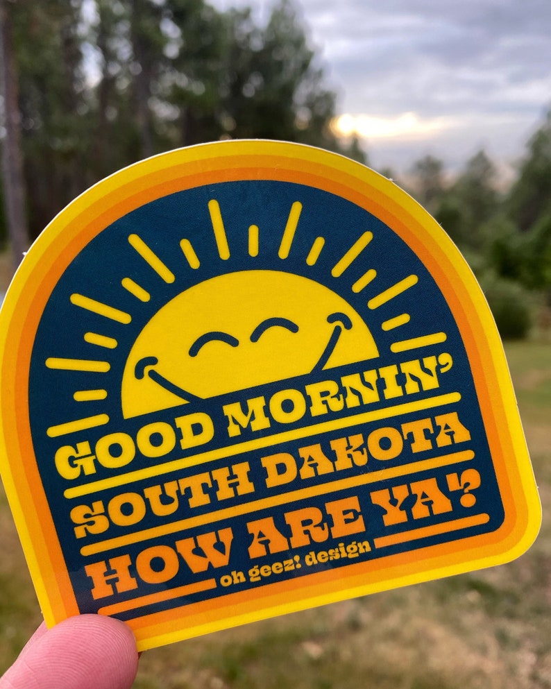 May include: Yellow and blue sticker with a smiling sun and the text "Good Morning South Dakota How Are Ya?" with the words "oh geez! design" at the bottom.