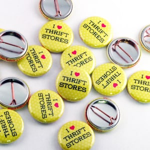Puede incluir: Una colección de botones amarillos con un patrón de lunares blancos. Cada botón presenta el texto "Me encantan las tiendas de segunda mano" con un símbolo de corazón rojo.