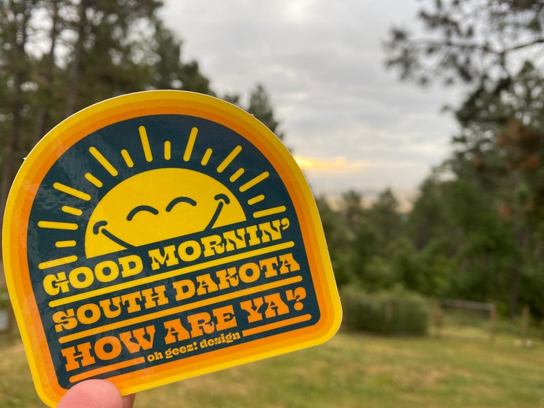 May include: A yellow and orange sticker with a smiling sun and the text "Good Morning South Dakota How Are Ya?"  oh geez! design