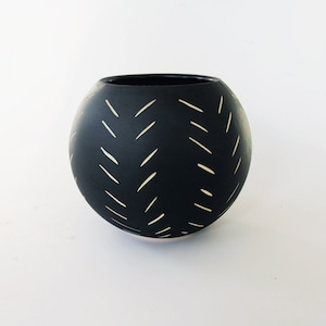May include: A black ceramic vase with a rounded shape. The vase features a pattern of diagonal, cream-colored lines. The interior of the vase is also black. The vase is sitting on a white surface.