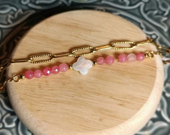 Könnte beinhalten: Ein goldenes Kettenarmband mit rosa Perlen und einem weißen Blumenanhänger. Das Armband liegt auf einer Holzoberfläche.