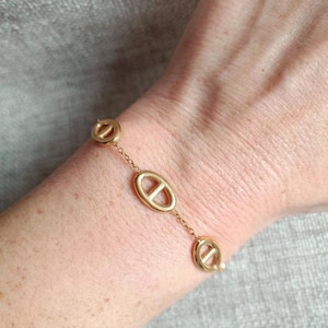 Peut inclure: Un bracelet doré composé de trois breloques ovales et circulaires reliées. Le bracelet est composé d'une chaîne délicate et se porte au poignet. Les breloques présentent un design distinctif, ajoutant une touche d'élégance au bijou.
