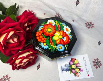 May include: A black, octagonal wooden box decorated with a colourful floral pattern in red, orange, yellow, and blue. Beside it are red roses and a card with a tulip illustration and the text "Hand Made with love."