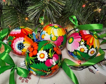 May include: Four hand-painted Christmas baubles with floral designs. Each bauble features a different colour scheme, including red, yellow, pink, and green, with intricate flower patterns. Green ribbons are attached for hanging, set against a Christmas tree background.