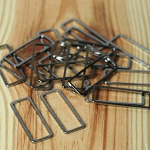 May include: A pile of silver metal rectangular rings, some are stacked on top of each other, on a light brown wooden surface.
