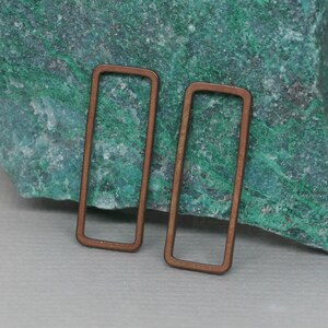 May include: Two rectangular copper-coloured metal earring hoops. The hoops are open and have a smooth, polished finish.