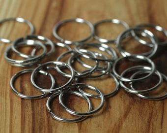 May include: A collection of shiny, silver-colored key rings, scattered on a wooden surface. The rings are circular, with a split for attaching keys or other items. The background is a warm, light brown wood grain.