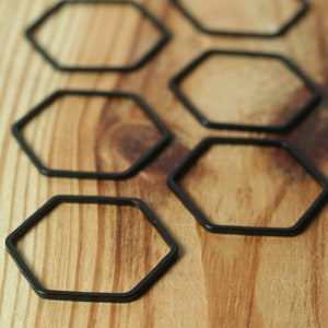 May include: Six black hexagonal rings arranged in a staggered pattern on a wooden surface.