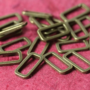 May include: A pile of antique gold-toned metal D-rings. The rings are rectangular in shape and have a smooth, polished finish.