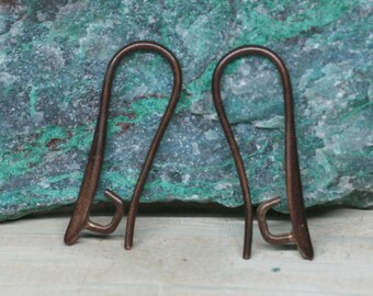 May include: Two copper-colored ear wires, each with a curved top and a small hook at the bottom. The ear wires are displayed against a background of green and blue stone.