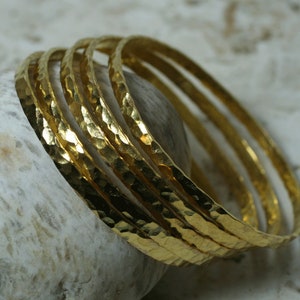 May include: Set of five gold-toned hammered metal bangles. The bangles are stacked on top of each other and have a textured surface.