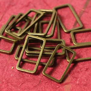 May include: A pile of antique gold-toned metal rectangular jump rings. The rings are of various sizes and are arranged in a random pattern.