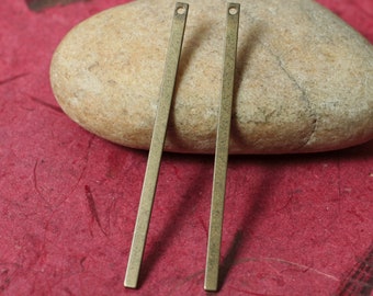 May include: Two antique brass-colored, rectangular bar pendants with small holes at the top. The pendants are displayed on a beige stone against a red background. These are ideal for jewelry making.