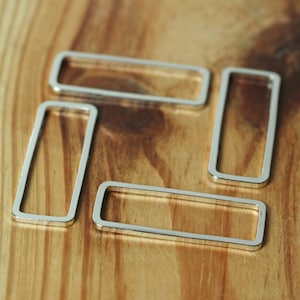 May include: Four silver metal rings of different sizes, arranged in a square shape on a wooden surface.