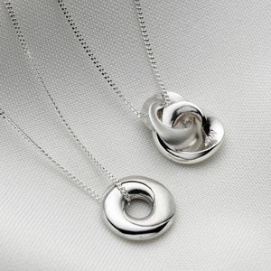 May include: Two silver necklaces with different pendant designs. One pendant is a circle with a smaller circle inside. The other pendant is a knot of three intertwined circles.