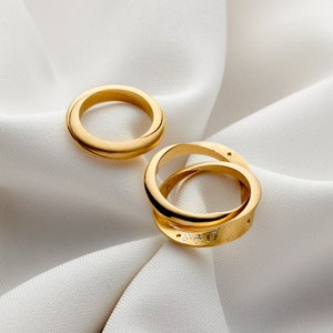 May include: Two gold wedding bands on a white fabric background. The bands are simple and elegant, with a smooth finish.