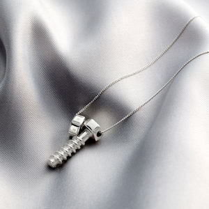 May include: A silver necklace with a screw and nut pendant. The screw is threaded and the nut is attached to the screw.