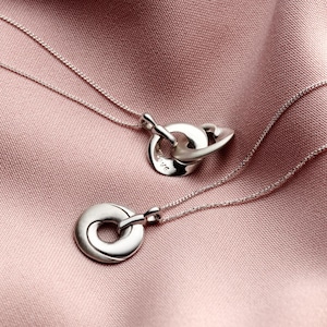 May include: Two silver necklaces with interlocking circle pendants. The larger pendant has the word "love" engraved on it.