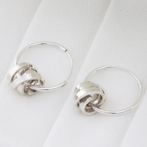 May include: A pair of silver hoop earrings with a twisted knot design. The hoops are simple and the knots are intricate.