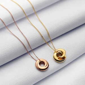 May include: Two gold necklaces with pendant charms. One necklace has a rose gold charm and the other has a gold charm. Both charms are in the shape of a circle.