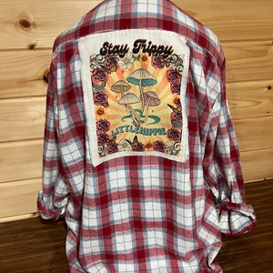 May include: Red and white plaid flannel shirt with a patch on the back that says "Stay Trippy" and features a mushroom design with the text "Little Hippie".
