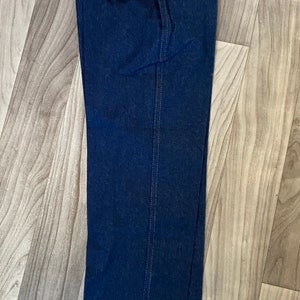 May include: A pair of dark blue denim jeans with a yellow and red label that reads "Rustler Brand An American Tradition" in the back pocket.