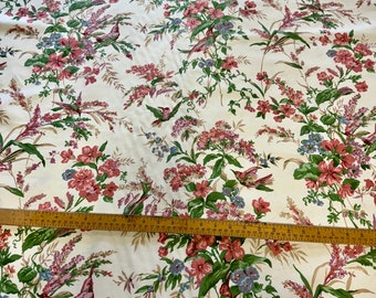May include: Cream-colored fabric with a floral and bird pattern. The design features pink, red, and blue flowers, green leaves, and hummingbirds. A wooden ruler is placed across the fabric, showing measurements in inches.