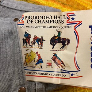 Puede incluir: Un folleto blanco y azul con el texto "ProRodeo Hall of Champions and Museum of the American Cowboy" y una estrella roja, blanca y azul. El folleto tambi&eacute;n tiene un logotipo rojo y blanco que dice "ProRodeo" con una peque&ntilde;a imagen de un vaquero montando un caballo. El folleto tiene im&aacute;genes de vaqueros montando caballos y un toro.