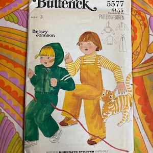 May include: A vintage sewing pattern for children's clothing. The pattern is for a green jumpsuit with a hood and a yellow and white striped shirt with overalls. The pattern is from Butterick and is number 5577. The pattern is sized for moderate stretch knits only.