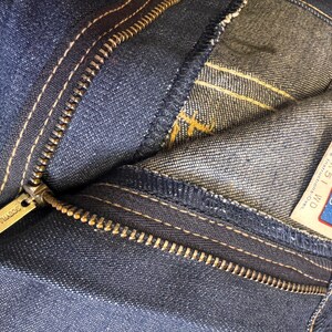 May include: Close-up of blue denim jeans with a visible zipper and white stitching. The zipper pull is gold-colored and has the brand name "SCOVILL" engraved. A tag with the text "Kids" and size "10" is visible.