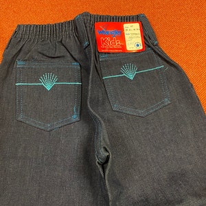 K&ouml;nnte beinhalten: Eine dunkelblaue Jeanshose mit einem blauen Stickmuster auf den Ges&auml;&szlig;taschen. Die Hose hat einen Bund mit Gummizug und ein Etikett mit der Aufschrift "Wrangler Kids".