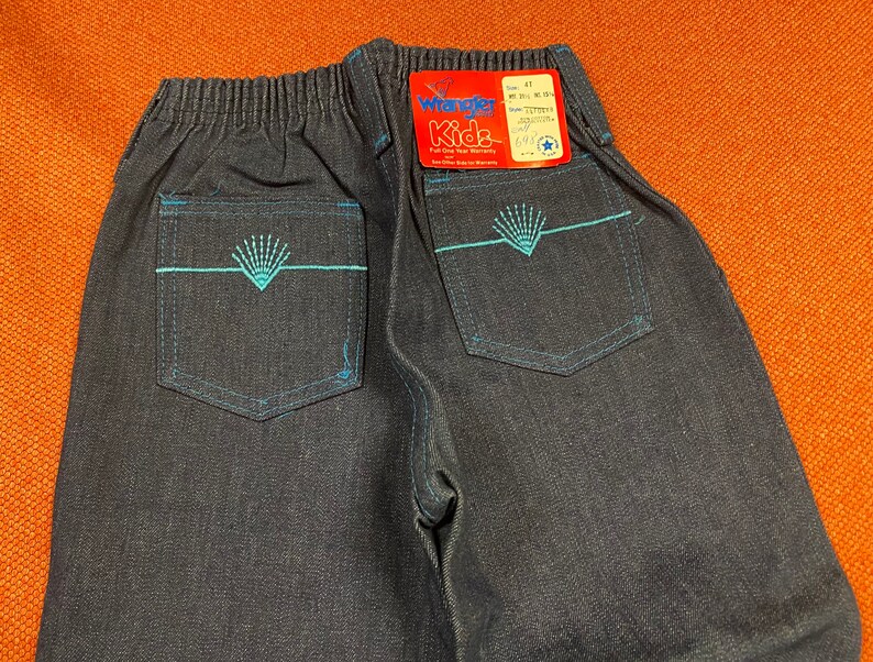 K&ouml;nnte beinhalten: Eine dunkelblaue Jeanshose mit einem blauen Stickmuster auf den Ges&auml;&szlig;taschen. Die Hose hat einen Bund mit Gummizug und ein Etikett mit der Aufschrift "Wrangler Kids".