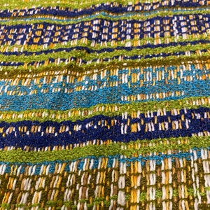 May include: Close-up of a woven fabric with a striped pattern in shades of green, blue, and yellow.