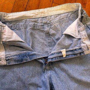 May include: Light blue denim jeans with an elastic waistband and a zipper fly. The waistband has a striped pattern. The jeans are unbuttoned, showing the interior lining and a small tag.
