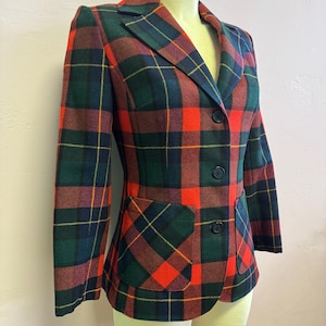 May include: A plaid blazer in a classic style. The jacket features a vibrant pattern of red, green, and navy blue with yellow accents. It has a notched collar, two front pockets, and black buttons. The blazer is displayed on a mannequin.