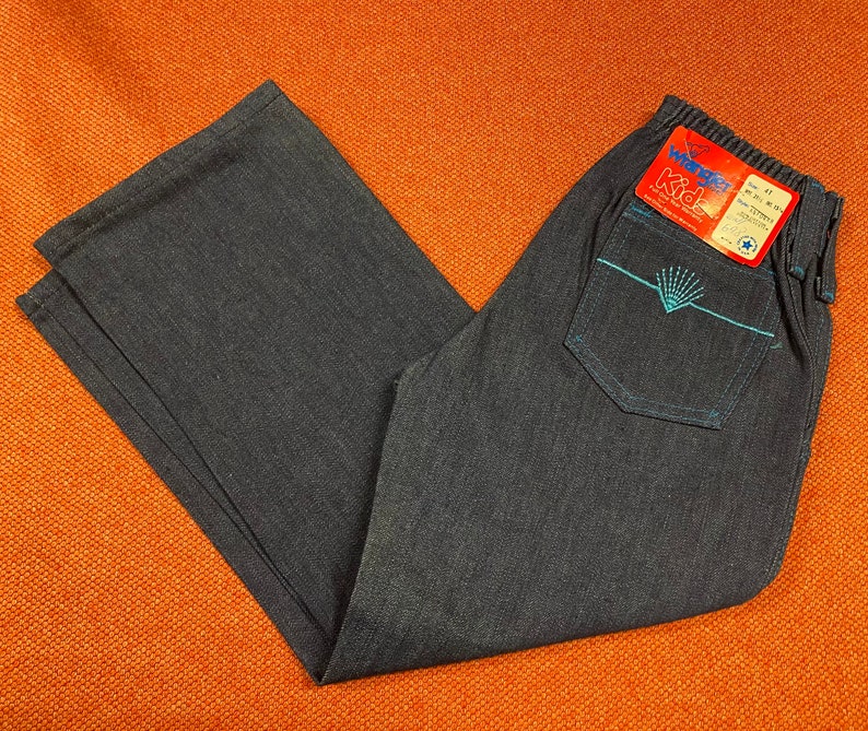 K&ouml;nnte beinhalten: Eine dunkelblaue Jeanshose mit einem blauen und wei&szlig;en Stickmuster auf der Ges&auml;&szlig;tasche. Die Hose hat einen Bund mit einem Etikett, auf dem "Wonder Kid" und "Gr&ouml;&szlig;e 4T" steht.