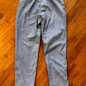 May include: Light blue denim jeans with a high waist and a classic straight leg fit. The jeans have a button and zipper closure, belt loops, and pockets. The back view shows the stitching details and the overall shape of the pants.