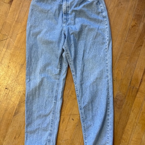 May include: Light blue denim jeans with an elastic waistband and a button closure. The jeans have a classic five-pocket design and a relaxed fit. The denim is a medium wash, and the jeans appear to be vintage.