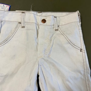 K&ouml;nnte beinhalten: Wei&szlig;e Jeanshose mit braunen N&auml;hten und einem kupferfarbenen Knopf. Die Hose hat einen klassischen F&uuml;nftaschen-Stil.