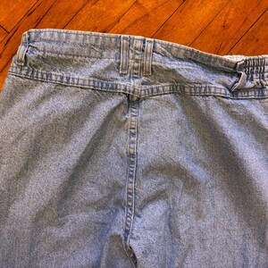 May include: Light blue denim jeans, viewed from the back. The jeans feature a high waist, belt loops, and a partially elastic waistband. The fabric has a faded appearance, with visible stitching details.