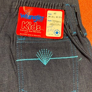 K&ouml;nnte beinhalten: Wrangler Kids blaue Jeans aus Denim mit einem blauen, gestickten Taschendetail. Das Etikett lautet "Wrangler Kids" und enth&auml;lt Gr&ouml;&szlig;en- und Stilinformationen. Das Etikett enth&auml;lt auch die Aufschrift "Volle einj&auml;hrige Garantie" und "Siehe R&uuml;ckseite f&uuml;r die Garantie".