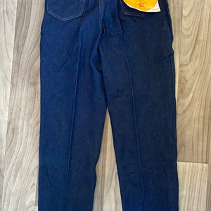 May include: A pair of dark blue denim jeans with a Rustler brand label on the back pocket. The label reads "Rustler Brand An American Tradition."