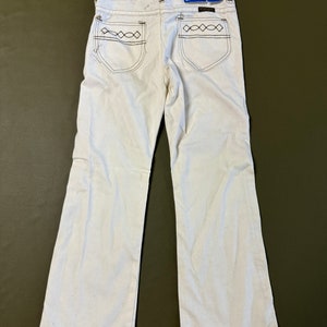 K&ouml;nnte beinhalten: Wei&szlig;e Schlaghose mit braunen N&auml;hten an den Ges&auml;&szlig;taschen. Die Hose hat ein Wrangler-Etikett am hinteren Bund.