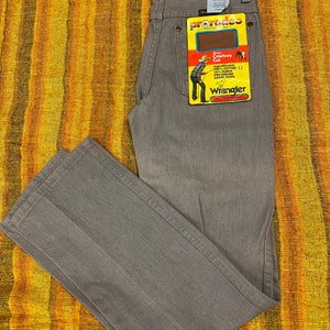Puede incluir: Vaqueros Wrangler grises con una etiqueta roja y amarilla que dice "Boys Cowboy Cut" y "Wrangler".