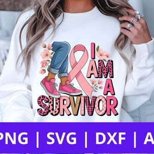 Peut inclure: Sweat-shirt blanc avec un ruban rose, les mots "I AM A SURVIVOR", et un graphisme de jambes en jean bleu et baskets roses. Le texte est dans différentes polices et motifs. Des fleurs roses sont également incluses.